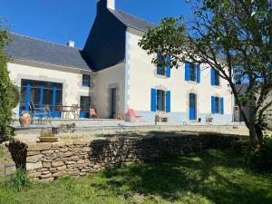 Casa blanca grande con ventanas azules y pared de piedra. en Le clos de Lisa en Clohars-Carnoët