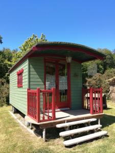 a small green house with red windows and a porch at Roulotte coin de nature in Lannion