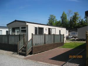 a small white house with a wooden fence at 119 Brigham Holiday Park. in Cockermouth