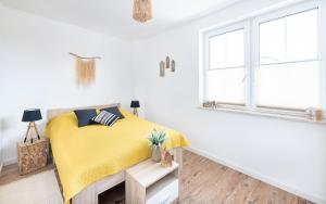 a white bedroom with a yellow bed and a window at Apartament Latarnika in Jarosławiec