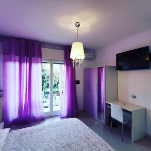 1 dormitorio con cortinas moradas, escritorio y cama en Ai Giardini Rooms, en Verona