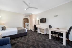a hotel room with a bed, table, television and chairs at Heritage Motor Inn Corowa in Corowa