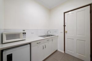 a white kitchen with a microwave and a sink at Heritage Motor Inn Corowa in Corowa