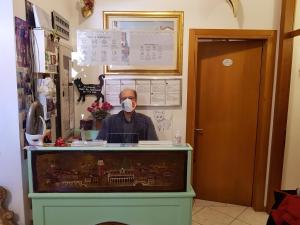 un homme portant un masque derrière un comptoir dans l'établissement Hotel Adua, à Venise