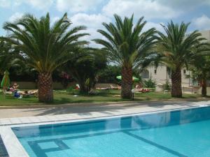 einen Pool mit Palmen und auf dem Gras liegenden Menschen in der Unterkunft Theoni Apartments in Malia