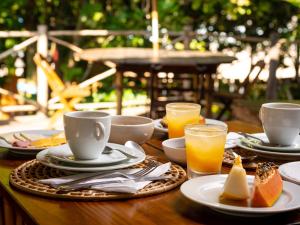 een houten tafel met borden en glazen sinaasappelsap bij Pousada Canto Bravo in Ilhabela
