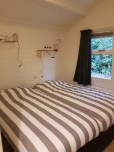 a bedroom with a striped bed with a window at Bospark De Schaapskooi in Epe