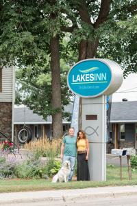 un hombre y una mujer de pie junto a un cartel con un perro en Lakes Inn en Detroit Lakes