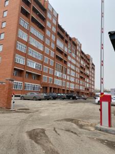 un gran edificio de ladrillo con coches aparcados en un aparcamiento en VIP-апартаменты в элитной новостройке. en Pavlodar