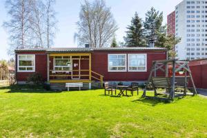 een klein rood huis met een speeltuin in een tuin bij Bungalow house flat in Rekola 33m2 in Vantaa