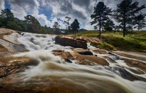 Un río con agua corriendo sobre rocas y árboles en Silverstone Lodge en Mbabane