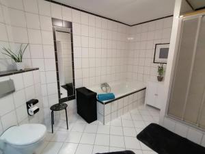 a white tiled bathroom with a tub and a toilet at Creek Inn, Contactless Check-in in Glanbrücken