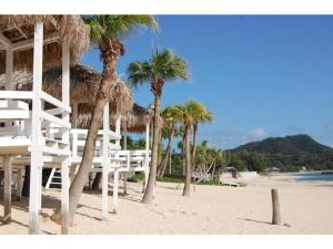 Amami Resort Bashayamamura - Vacation STAY 81977 في أمامي: شاطئ فيه نخيل وكراسي بيضاء على الشاطئ