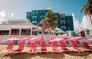 a bunch of pink chairs and umbrellas on a beach at The Tryst Beachfront Hotel in San Juan