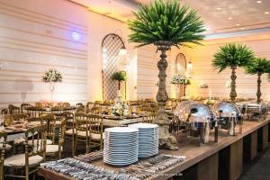 um salão de banquetes com mesas, cadeiras e palmeiras em Mercure Macae em Macaé