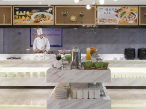 a chef standing behind a counter in a kitchen at Shenzhen Universide-Senter＆BaoHe Road Kyriad Marvelous Hotel in Shenzhen