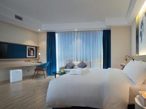 Habitación de hotel con cama blanca grande y escritorio. en Kyriad Mavelous Hotel Shantou Gurao, en Shantou