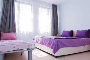 a bedroom with two beds with purple sheets and windows at Апартамент и студио Фантазия in Sozopol