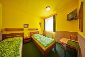 a yellow room with two beds and a table and a desk at Pension & restaurace Zelený Mlýn in Žacléř