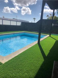 a swimming pool with green grass next to a house at Villa Altamosa in Yaiza