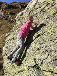 Ein kleines Mädchen klettert auf einen Felsen in der Unterkunft Haus Kibitz in Fieberbrunn