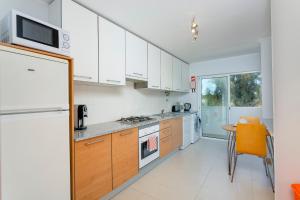 a kitchen with white cabinets and a table and a refrigerator at Cabanas Beach Penthouse in Cabanas de Tavira