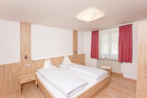 a bedroom with a large white bed with red curtains at Gasthof Huber in Braies