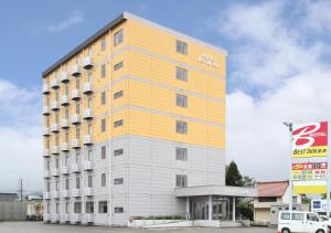 un edificio alto amarillo y blanco en un estacionamiento en Best Inn Uozu en Uozu