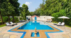 a swimming pool with lounge chairs and umbrellas at Sawai Madhopur Lodge - IHCL SeleQtions in Sawāi Mādhopur