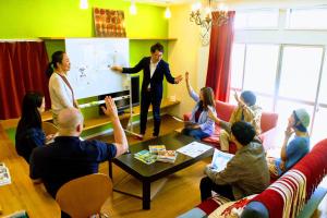 a group of people in a room with a man on a screen at ゲストハウス ルルル 最大12名可 合宿 大家族 団体旅行にオススメ in Kochi