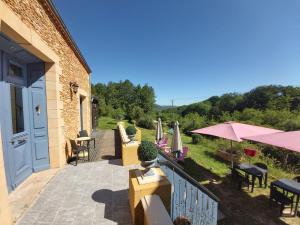 une terrasse avec des chaises, des tables et un parasol dans l'établissement BonBon Chambre d'hôtes, à Saint-Julien-de-Lampon