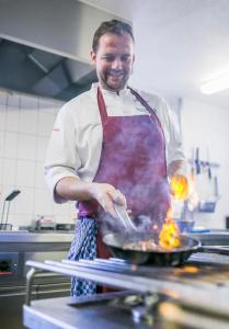 Ein Mann, der Essen in einer Pfanne in einer Küche kocht. in der Unterkunft Hotel-Restaurant Sennhütte im Herzen des Südschwarzwalds in Kleines Wiesental