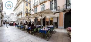grupa ludzi siedzących przy stołach z parasolami na ulicy w obiekcie Living Lisboa Baixa Apartments w Lizbonie