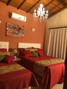 a bedroom with two beds with red sheets and a chandelier at Casa dos Mineiros in Arraial d'Ajuda