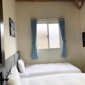 a bedroom with a bed and a window with blue curtains at Jinsha Vanilla Homestay in Nangan