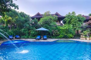 a swimming pool with two chairs and an umbrella at Sri Phala Resort & Villa in Sanur