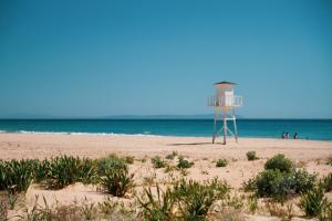 a lifeguard tower on a beach with people in the water at Hotel Avenida Playa in Zahara de los Atunes