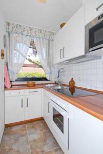 cocina con armarios blancos, fregadero y ventana en Ferienhaus Nordwind en Bensersiel