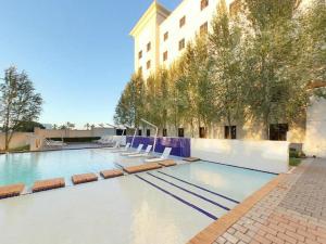 a large swimming pool with chairs and a building at Metcourt at Emperors Palace in Kempton Park