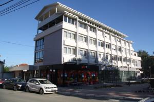 a white building with cars parked in front of it at Rooms S&S Milicevic u strogom centru Aleksandrovca in Aleksandrovac
