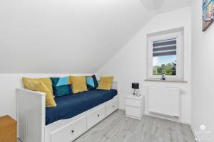 biała sypialnia z łóżkiem z niebieskimi i żółtymi poduszkami w obiekcie Jantar Apartamenty - Casa Francesco w Grzybowie