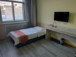a bedroom with a bed and a desk with a television at JUN Hotels Yulin Yuyang District Xinlou Store in Yulin