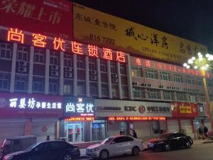 a building with neon signs and cars parked in front of it at Thank Inn Chain Hotel Shandong Dezhou Lingcheng District Lingzhou Road Ginza in Dezhou