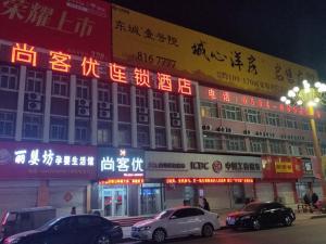 ein Gebäude mit Neonschildern und davor geparkt in der Unterkunft Thank Inn Chain Hotel Shandong Dezhou Lingcheng District Lingzhou Road Ginza in Dezhou