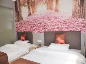two beds in a bedroom with pink flowers on the wall at JUN Hotels Jinzhong Yuci District Railway Station in Jinzhong