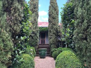 einen Garten mit einem Haus zwischen zwei großen Bäumen in der Unterkunft French Cottage Beechworth with stunning Alfresco Garden in Beechworth