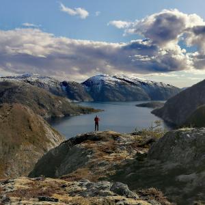 Ein Mann steht auf einem Berg mit Blick auf einen See. in der Unterkunft Velfjord Camping & Hytter in Velfjord