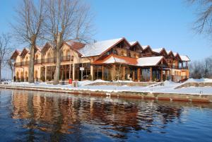a large house with snow on the side of a river at Hotel Roś in Pisz