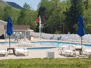 a swimming pool with chairs and umbrellas next to a pool at Town Square Condominiums in Waterville Valley
