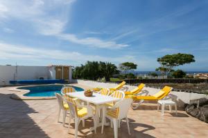um pátio com uma mesa e cadeiras ao lado de uma piscina em CASA AMARILLA sunny holiday home with heated pool em San Miguel de Abona